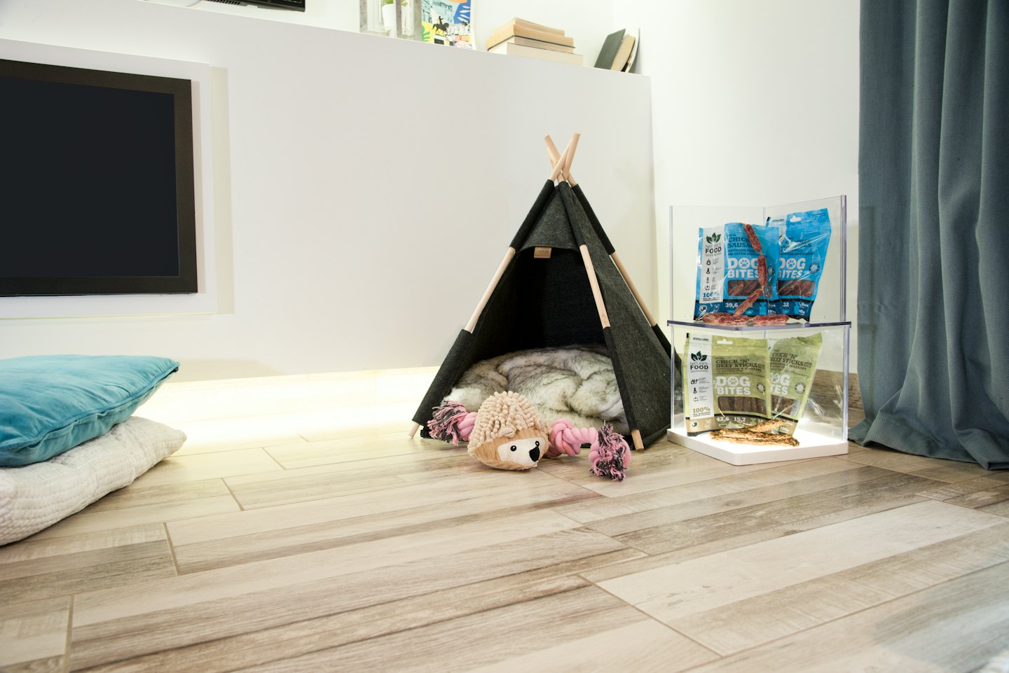 Una teepee grigia per animali domestici con giocattoli e snack sul pavimento.
