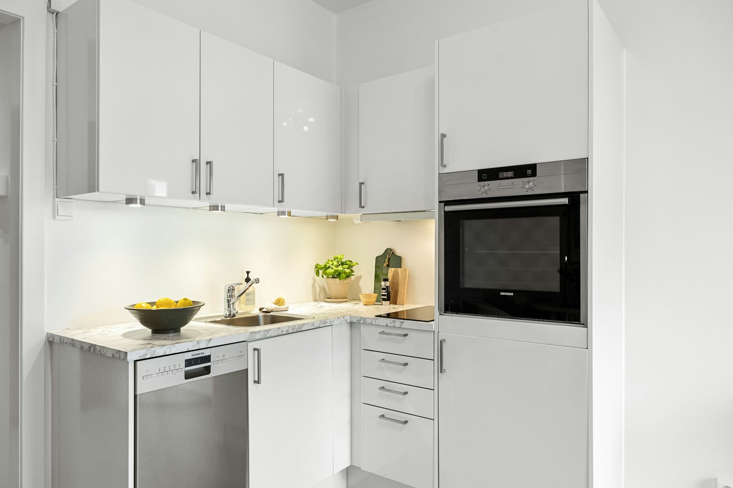 Cucina moderna con mobili bianchi e piano di lavoro in marmo.